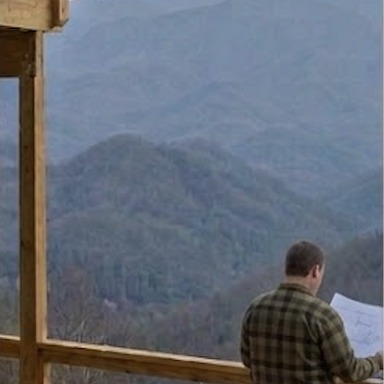 A Lodge Masters technician reviewing plans on a cabin deck overlooking the Smoky Mountains