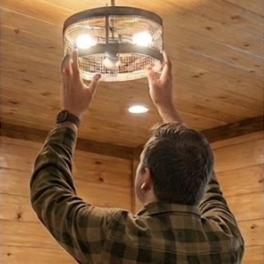A Lodge Masters technician installing a ceiling light fixture in a cabin bedroom