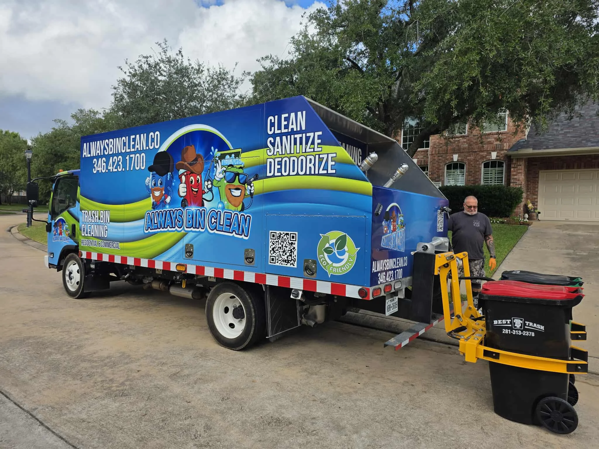 A brightly branded 'Always Bin Clean' large blue truck parked on a residential street next to a worker and bins, ready for cleaning service.