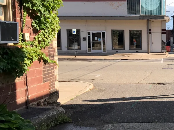 A brick building corner covered in ivy with a street and a commercial building with large windows in the background.