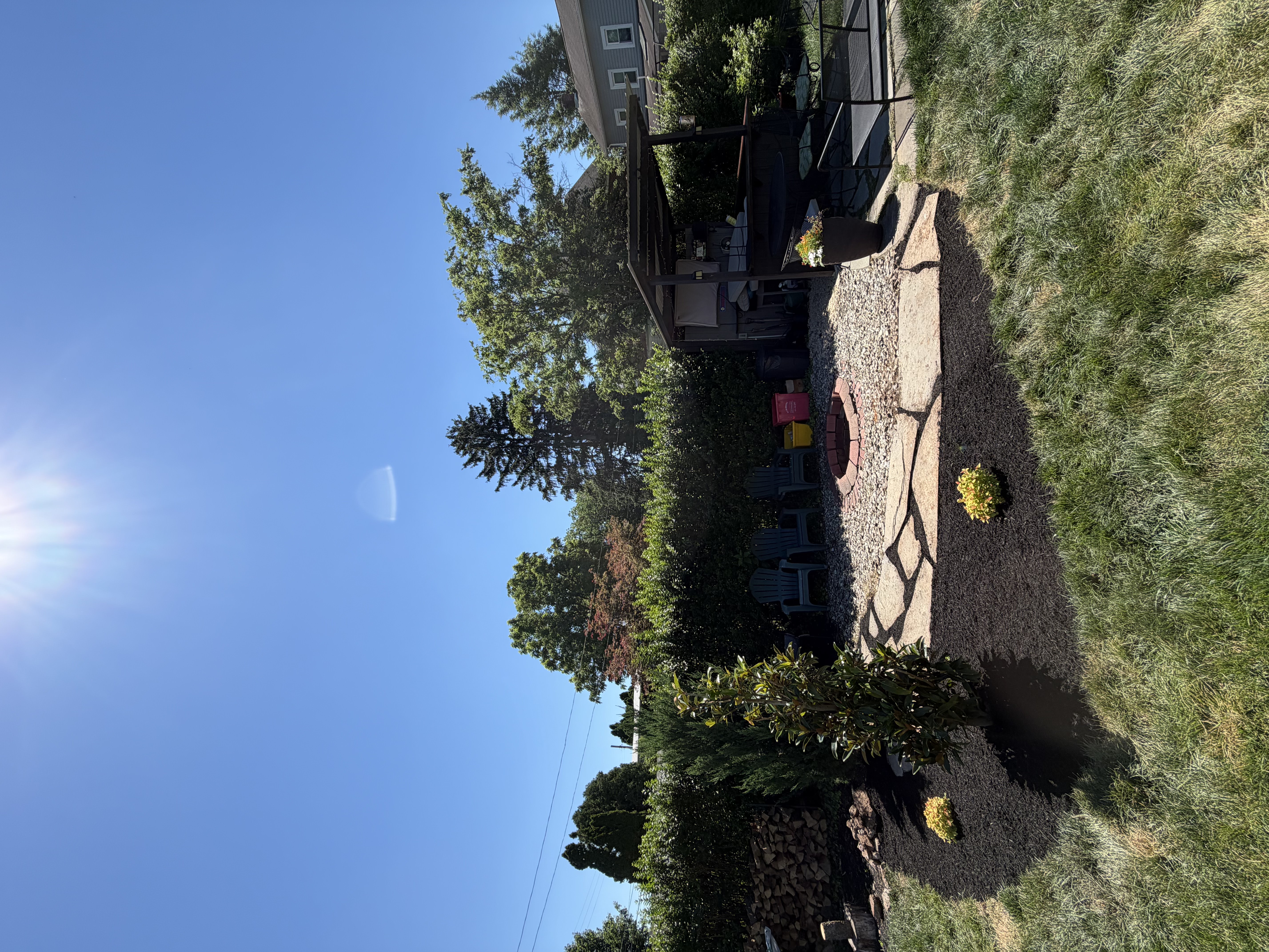 Backyard landscape design with a gravel fire pit area, flagstone border, flowering mulch beds, and privacy hedges.