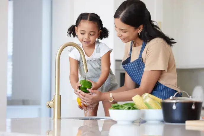 Family rinsing vegetables together at the kitchen sink