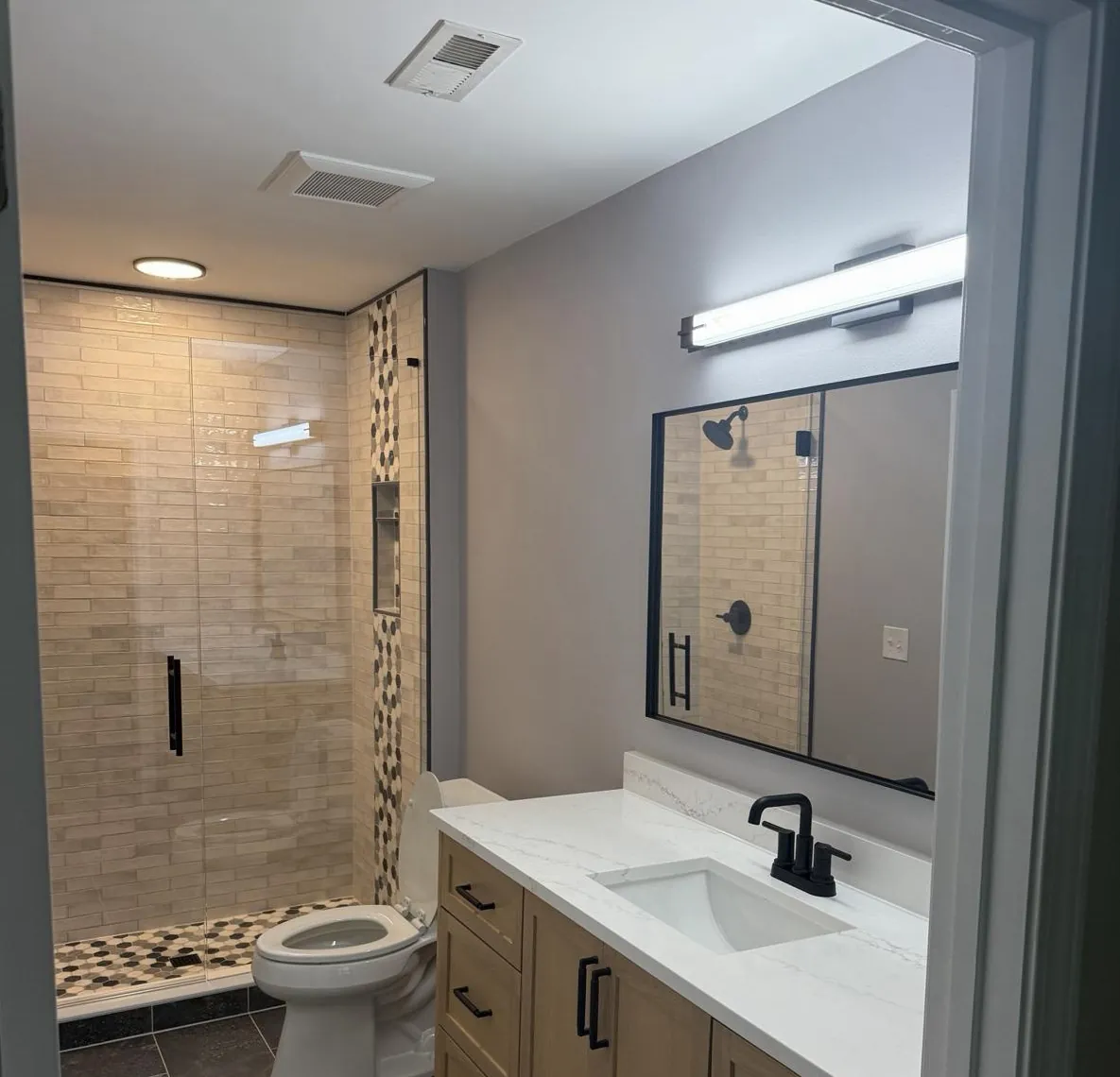 The same hall bathroom after the remodel, with a tiled walk-in shower, glass door, and new vanity