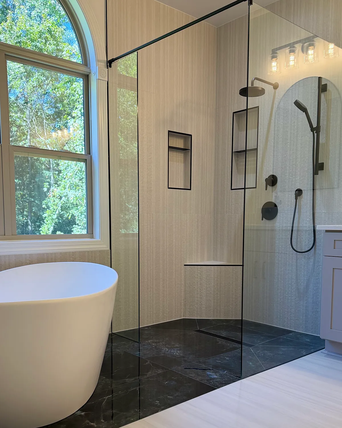 Walk-in shower with a frameless glass panel, recessed niches, corner bench, and dark marble-look floor tile