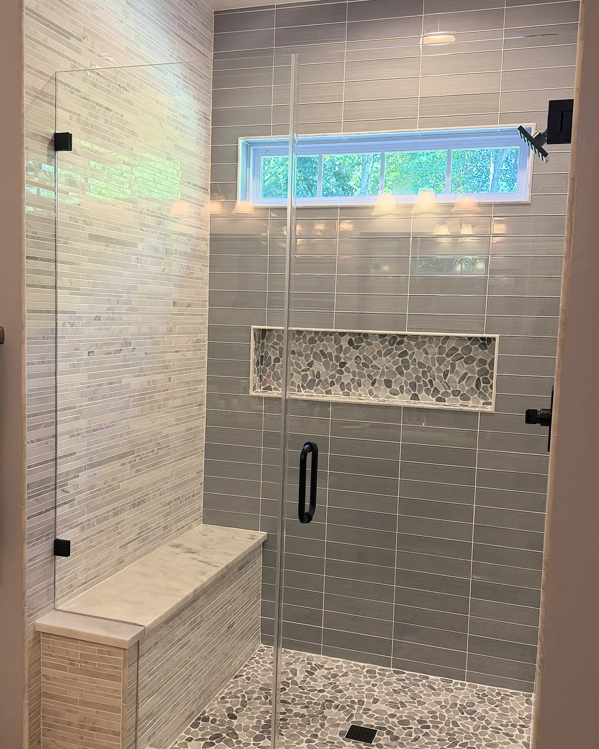 Glass-enclosed shower with a built-in bench, pebble floor, and long mosaic niche
