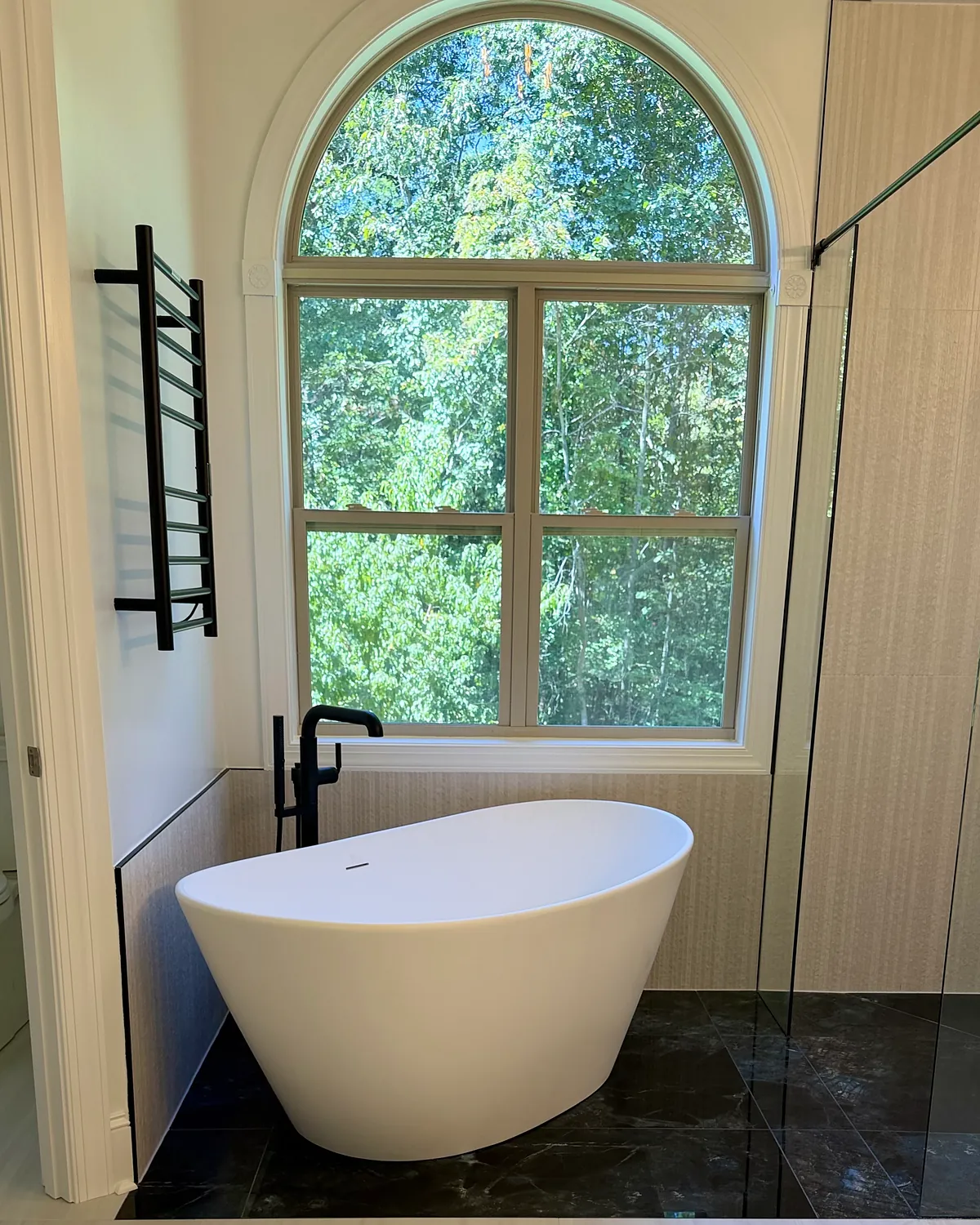 Freestanding soaking tub with a matte black floor-mounted faucet under an arched window