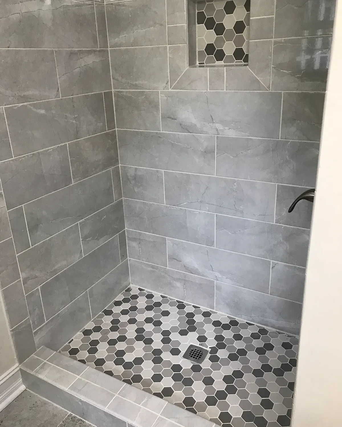 Walk-in shower with gray hexagon tile floor and a recessed niche