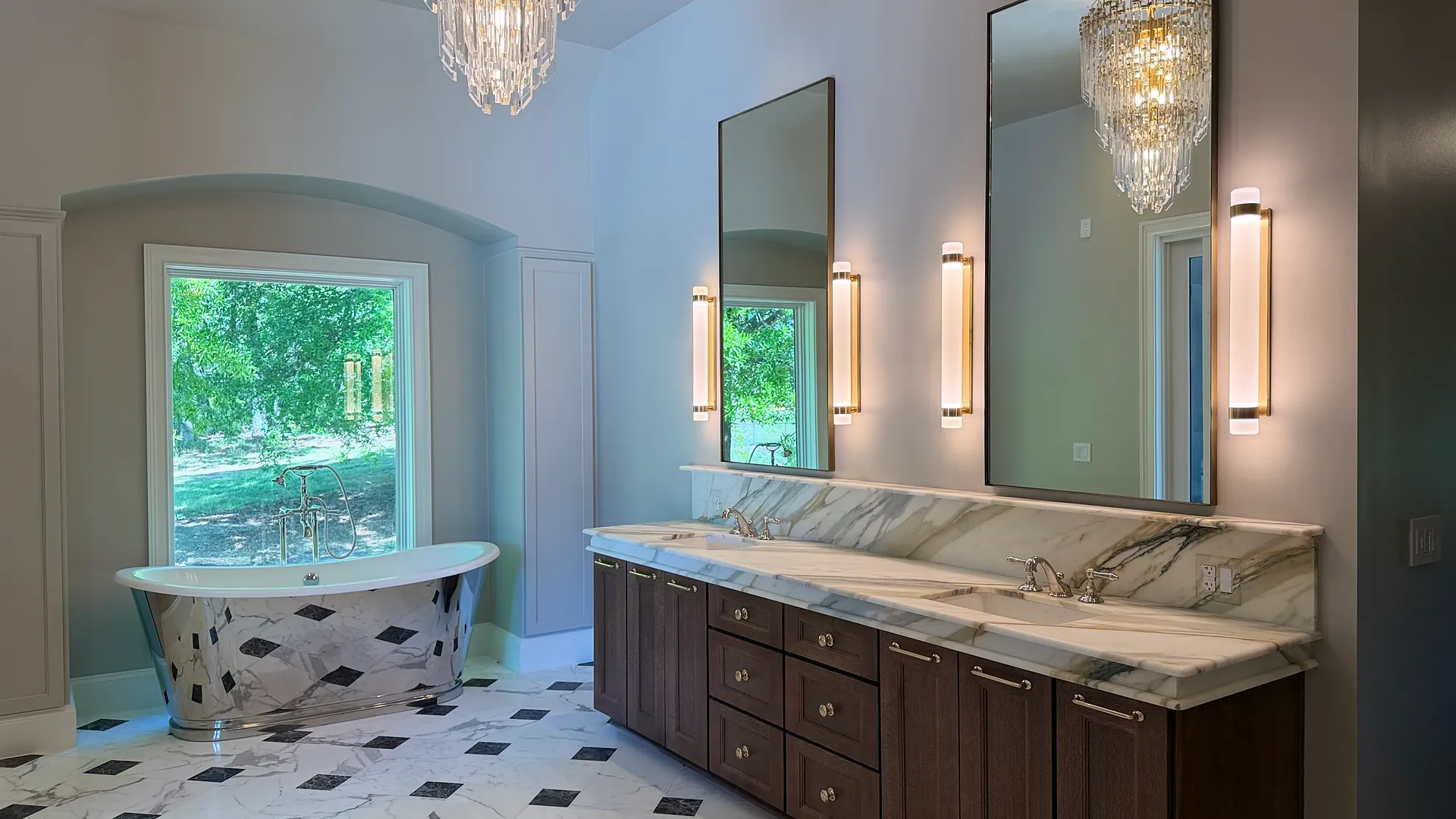 Primary bathroom with marble and black diamond tile floors, a polished metal freestanding tub, and a crystal chandelier