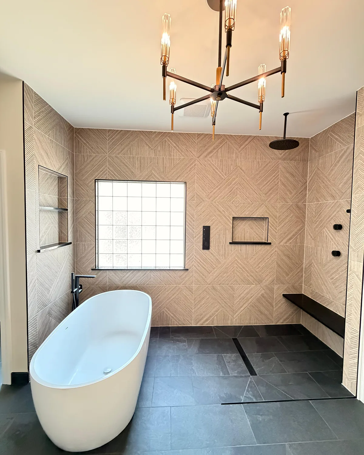 Primary bathroom with a freestanding tub, linear drain shower, floating bench, and modern chandelier