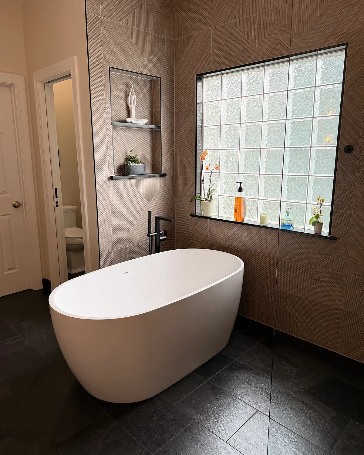 Freestanding soaking tub positioned beside a glass block window