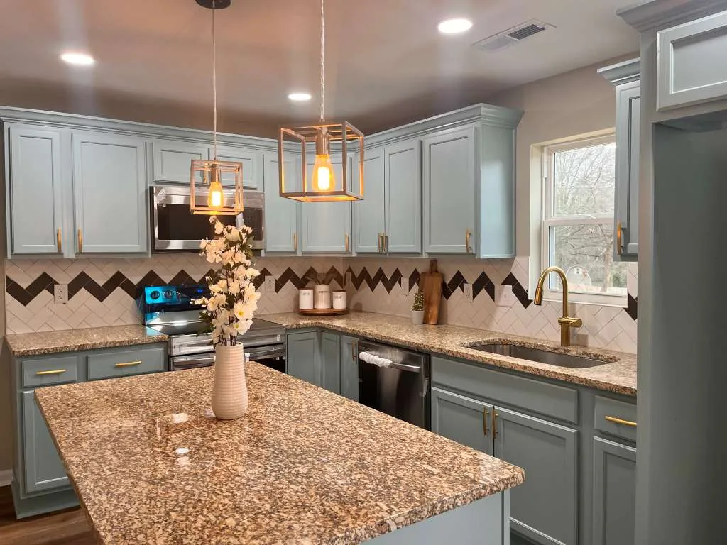 Kitchen with gray-blue cabinets, granite countertops, a chevron tile backsplash, and gold hardware