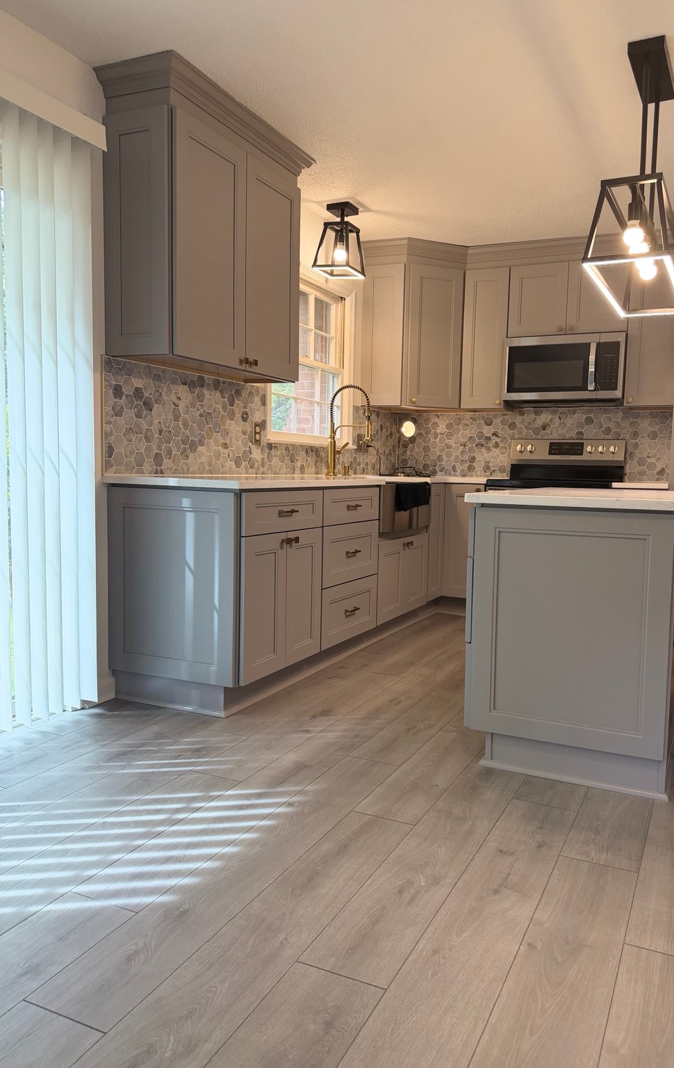 The same kitchen after remodeling, with gray cabinets, a white island and a hexagonal backsplash