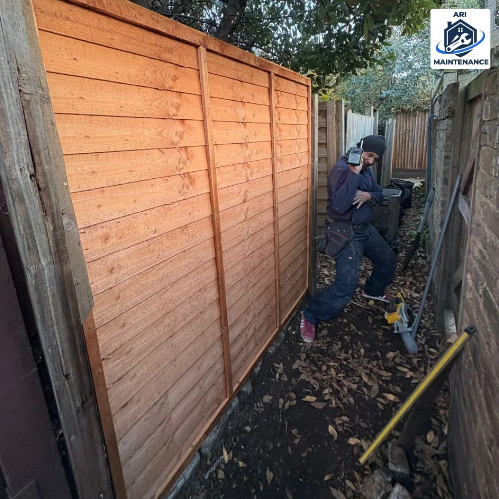 Worker installing wooden lap-fence panel, captured from the side mid-build.