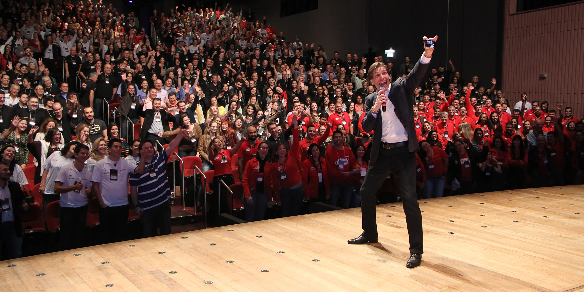 Fábio Marques no palco tirando uma selfie com uma plateia lotada de pé ao fundo