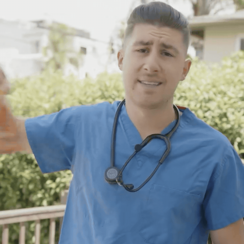 A nurse's stethoscope beside house keys and a small apartment building model, illustrating real estate income for healthcare workers
