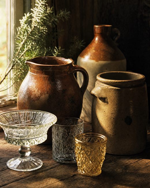 Redware and stoneware crocks beside pressed glass on a windowsill