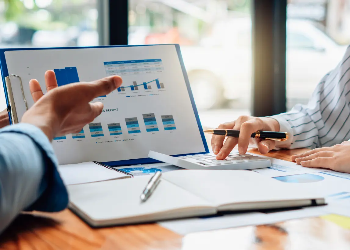 Two professionals reviewing marketing and print performance reports with charts and analytics on a laptop and clipboard during a business meeting at Elite Printing Group.