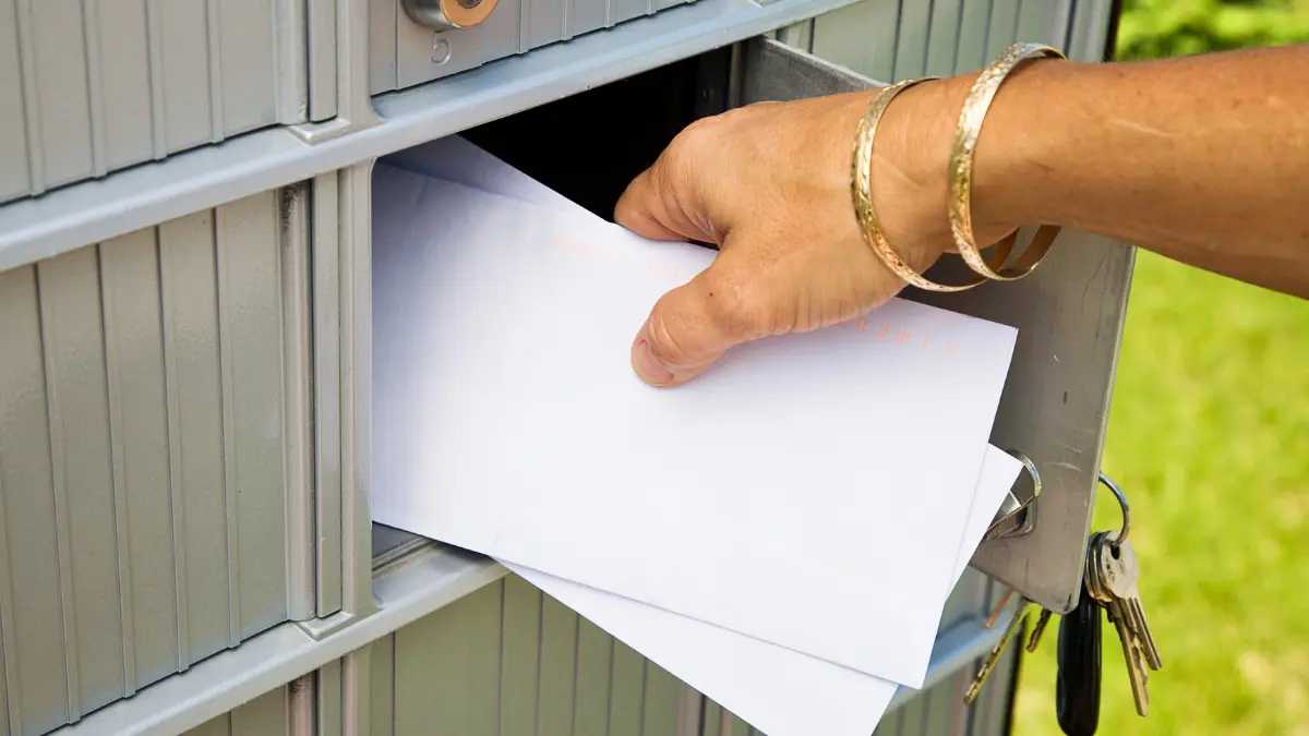 Person delivering direct mail envelopes into community mailboxes, representing Elite Printing Group’s targeted mailing and EDDM marketing services.