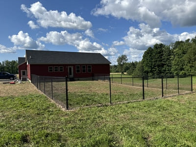 Black chain-link fence enclosing a backyard of a red house