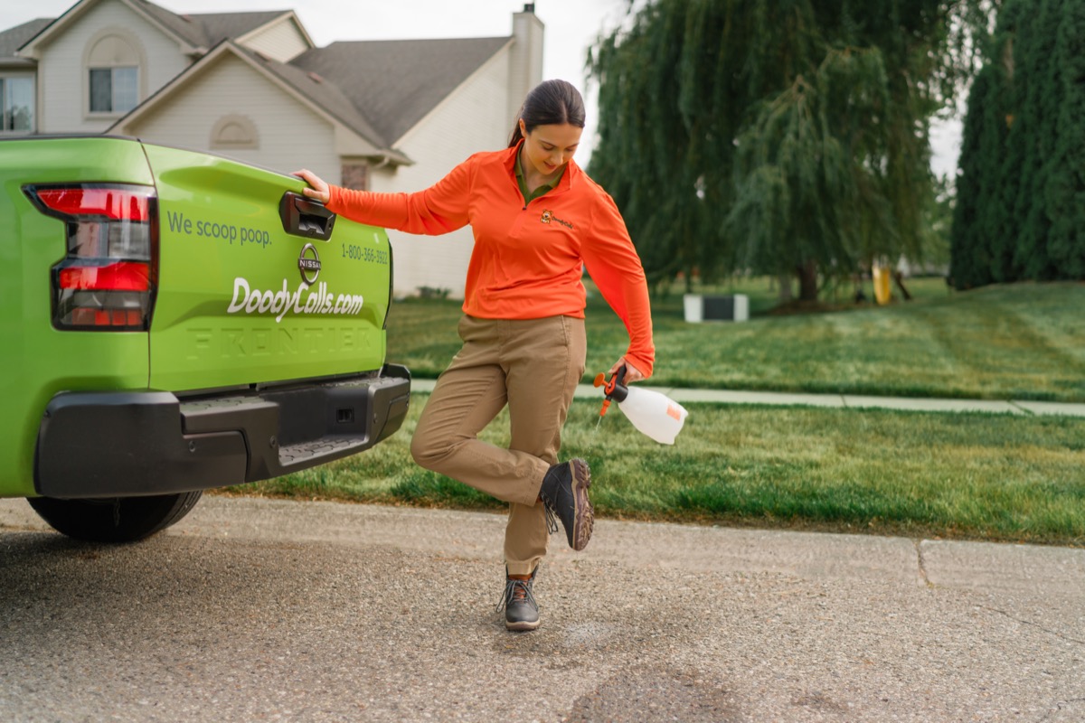 DoodyCalls technician applying yard deodorizer near a branded truck