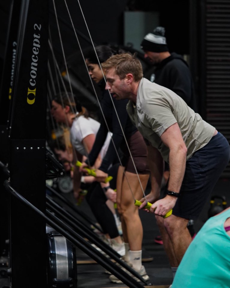A member mid-pull on the ski erg with a row of ski ergs behind
