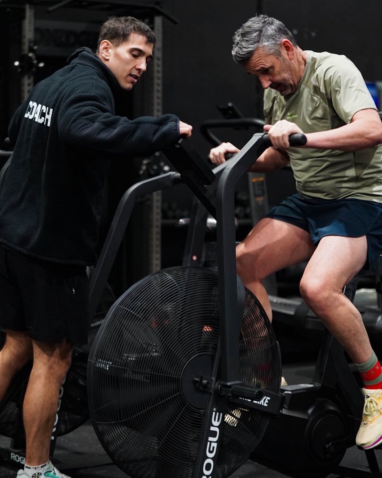 A coach leaning in to push a member on the assault bike