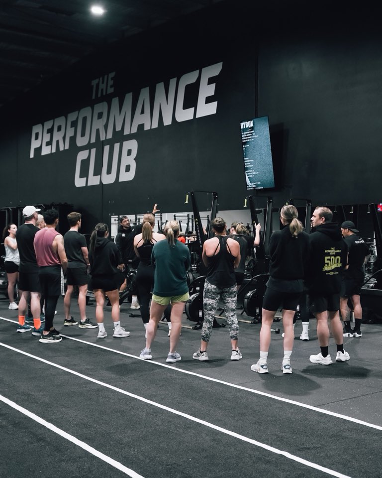 Members gathered on the track listening to a coach under the club sign
