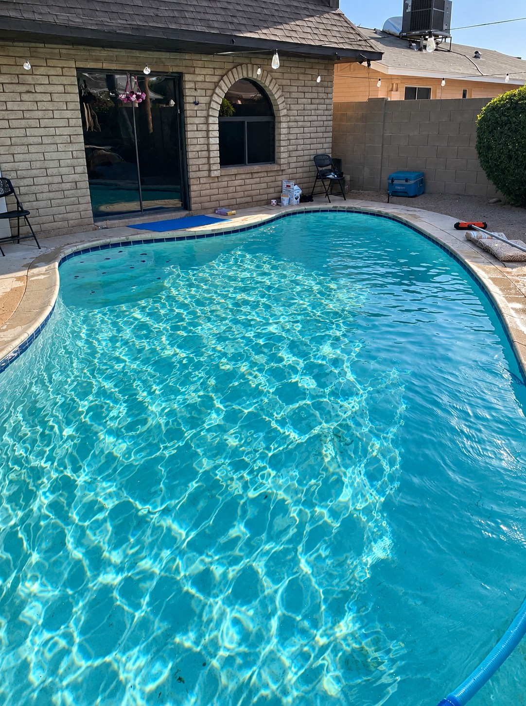 Clear blue swimming pool with string lights and landscaping after professional pool service