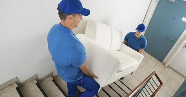 Two movers carrying a sofa up a staircase