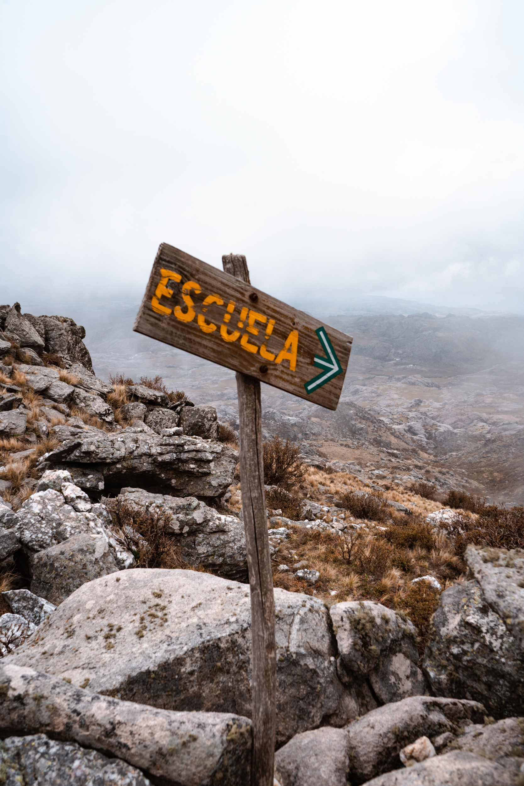 Cartel de madera en la montaña con la palabra Escuela y una flecha que señala el camino