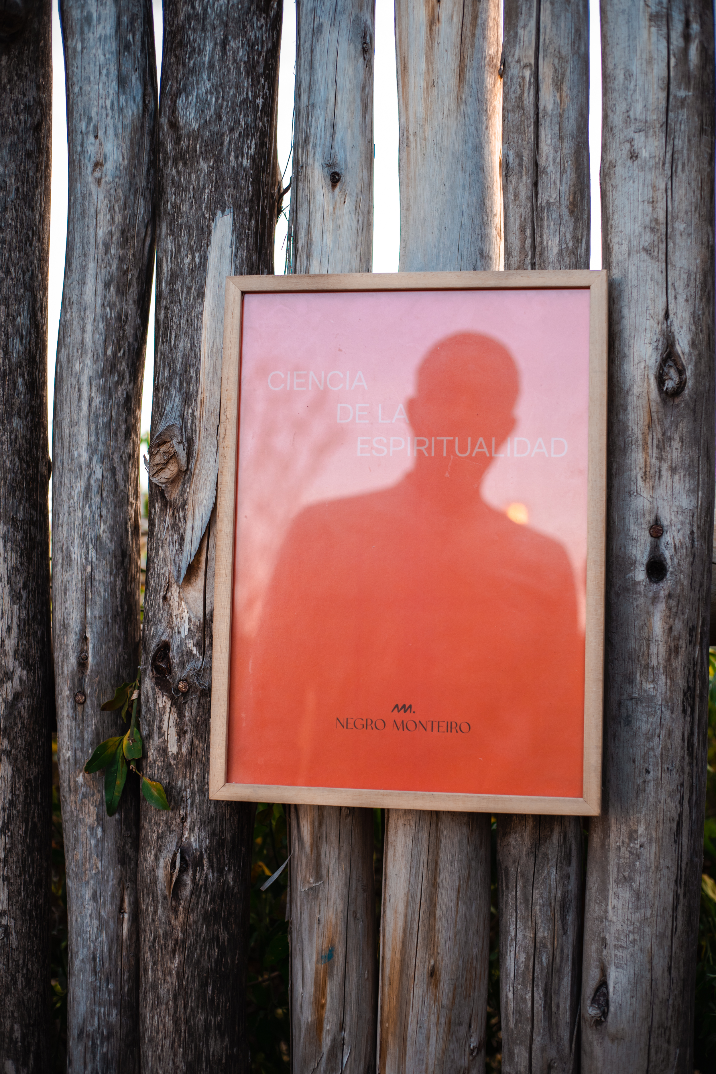 Póster enmarcado con la sombra del Negro Monteiro, colgado en una cerca de madera. Dice «Ciencia de la espiritualidad».