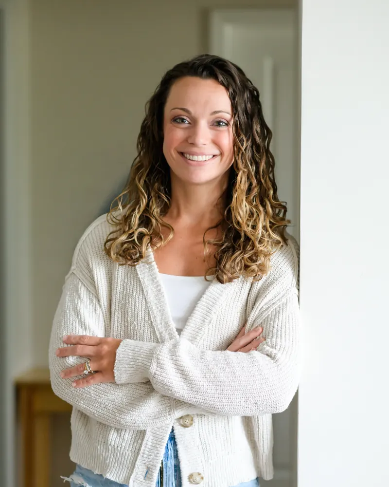 Jen Navon, functional health coach, smiling at the camera with her arms crossed in a cream cardigan