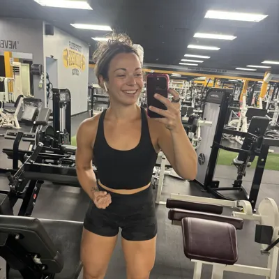 Jen in 2023, a smiling gym mirror selfie in a black sports top and shorts