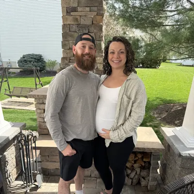 Jen, pregnant in 2024, smiling beside a bearded man on a back patio