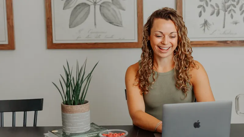 Jen Navon smiling on a video call at her desk, laptop open, botanical prints on the wall