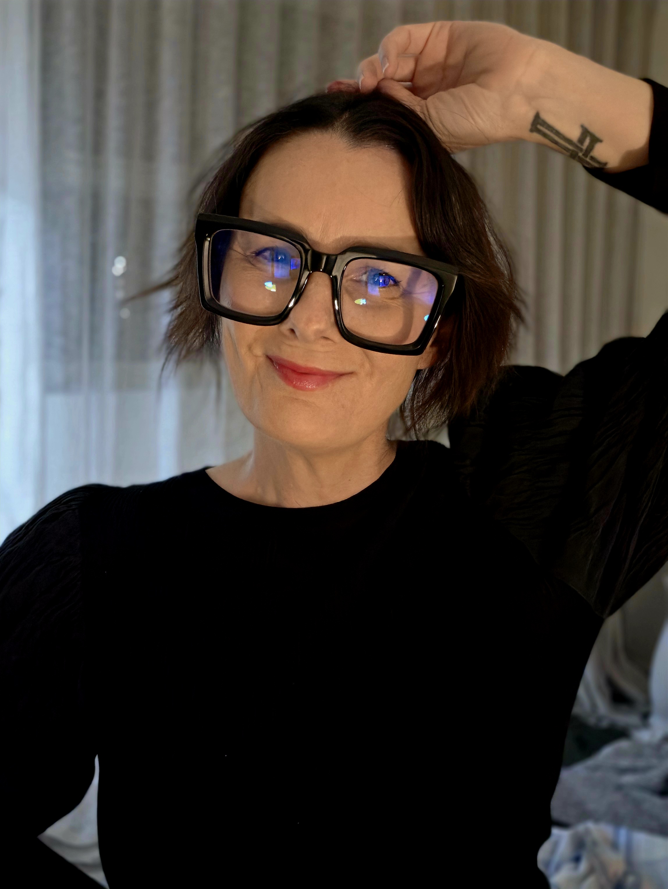 Ali Orchard smiling in oversized glasses, lipstick and a black jumper