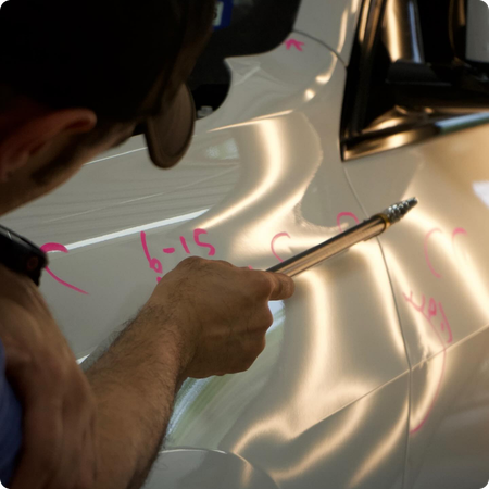 Technician repairing hail dents on car hood