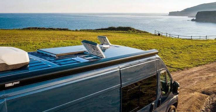 Open campervan rooflight with a coastal background