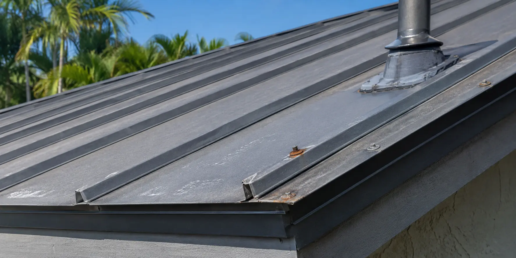Existing Florida metal roof showing coating wear, deteriorated fasteners and a flashing concern near a roof penetration