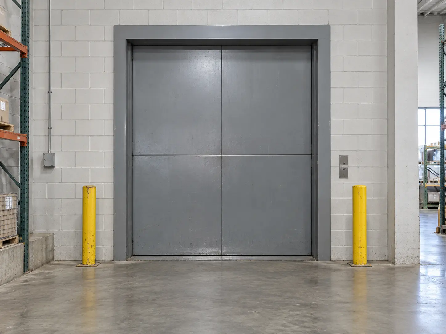 Industrial freight elevator with steel doors and yellow protective bollards.
