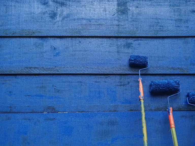 Three paint rollers resting on freshly painted blue wood siding
