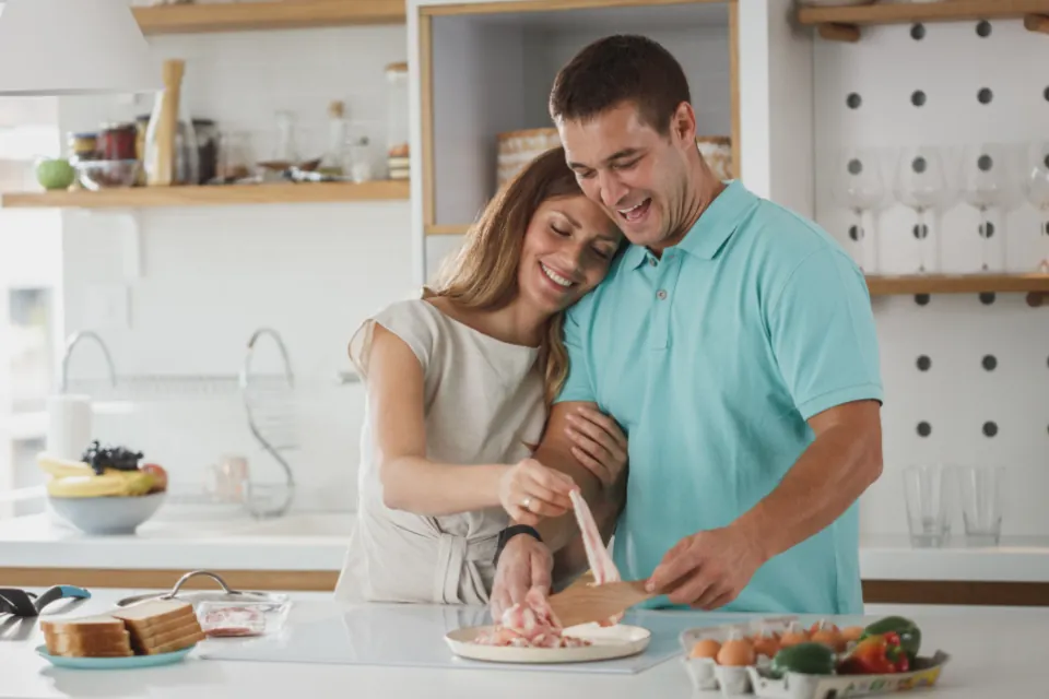 Couple laughing while cooking together in a bright white kitchen