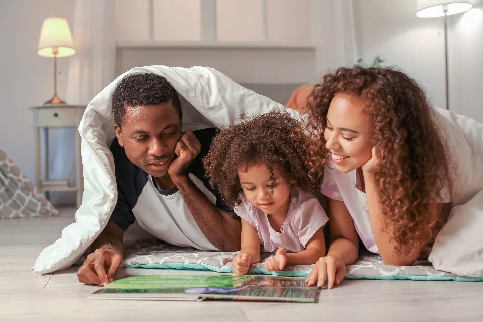 Parents and daughter reading together under a blanket at home