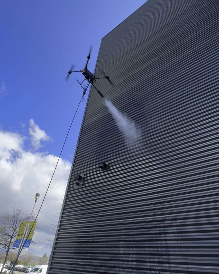 Drone soft-washing dark metal cladding on a dealership
