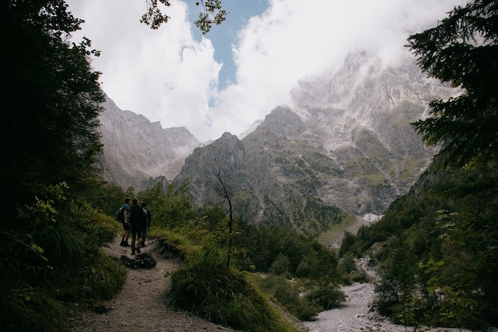 Group hiking through lush forest and rugged mountains under a dramatic sky - Sinitta Leunen Group hiking through lush forest and rugged mountains under a dramatic sky - Sinitta Leunen
