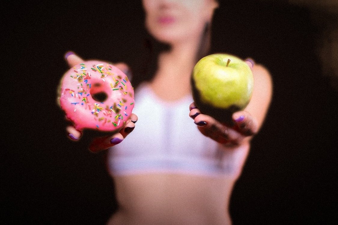 A woman holding a donut in one hand and an apple in the other