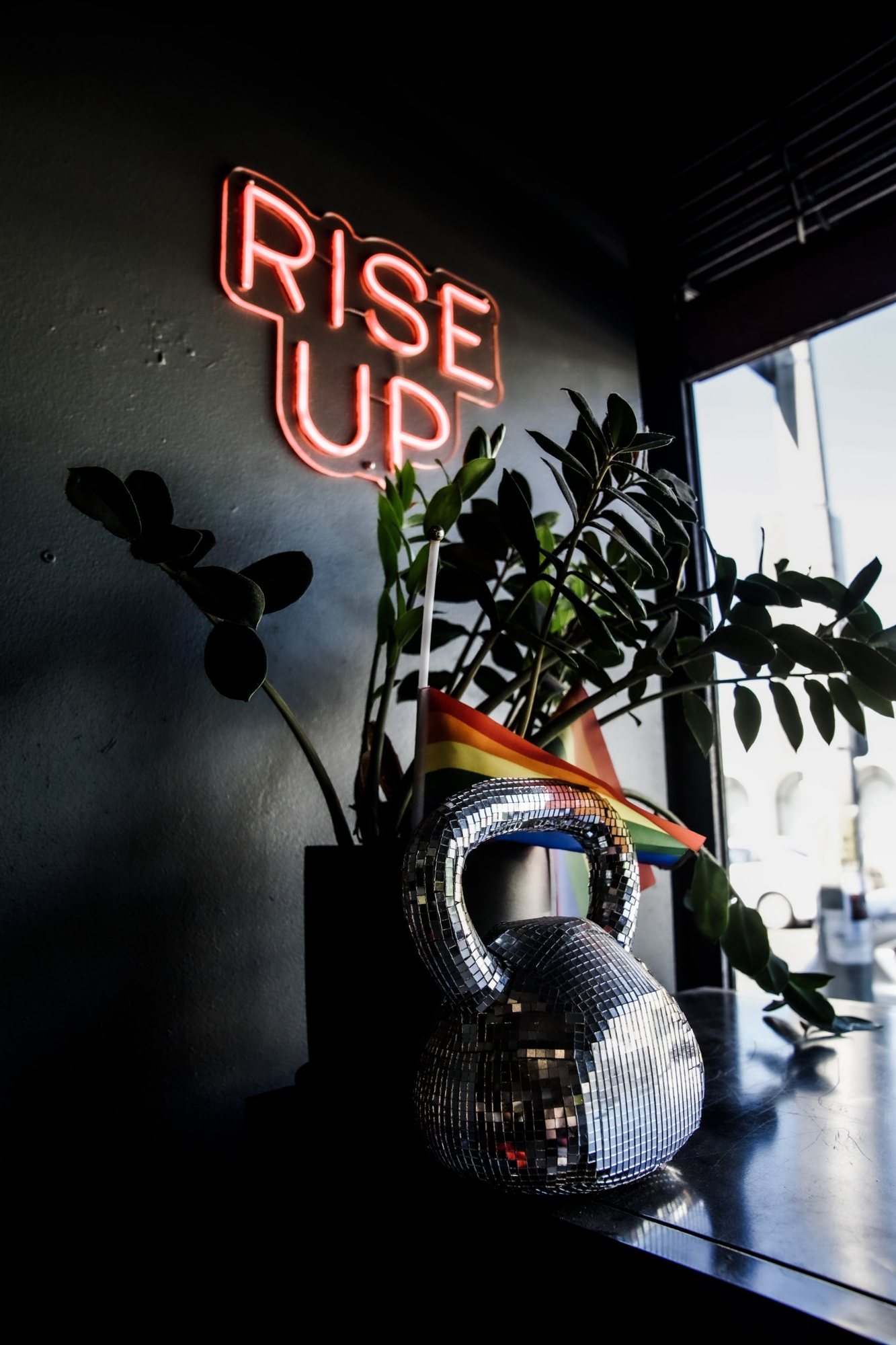 A disco ball kettlebell and a pride flag under the RISE UP neon sign