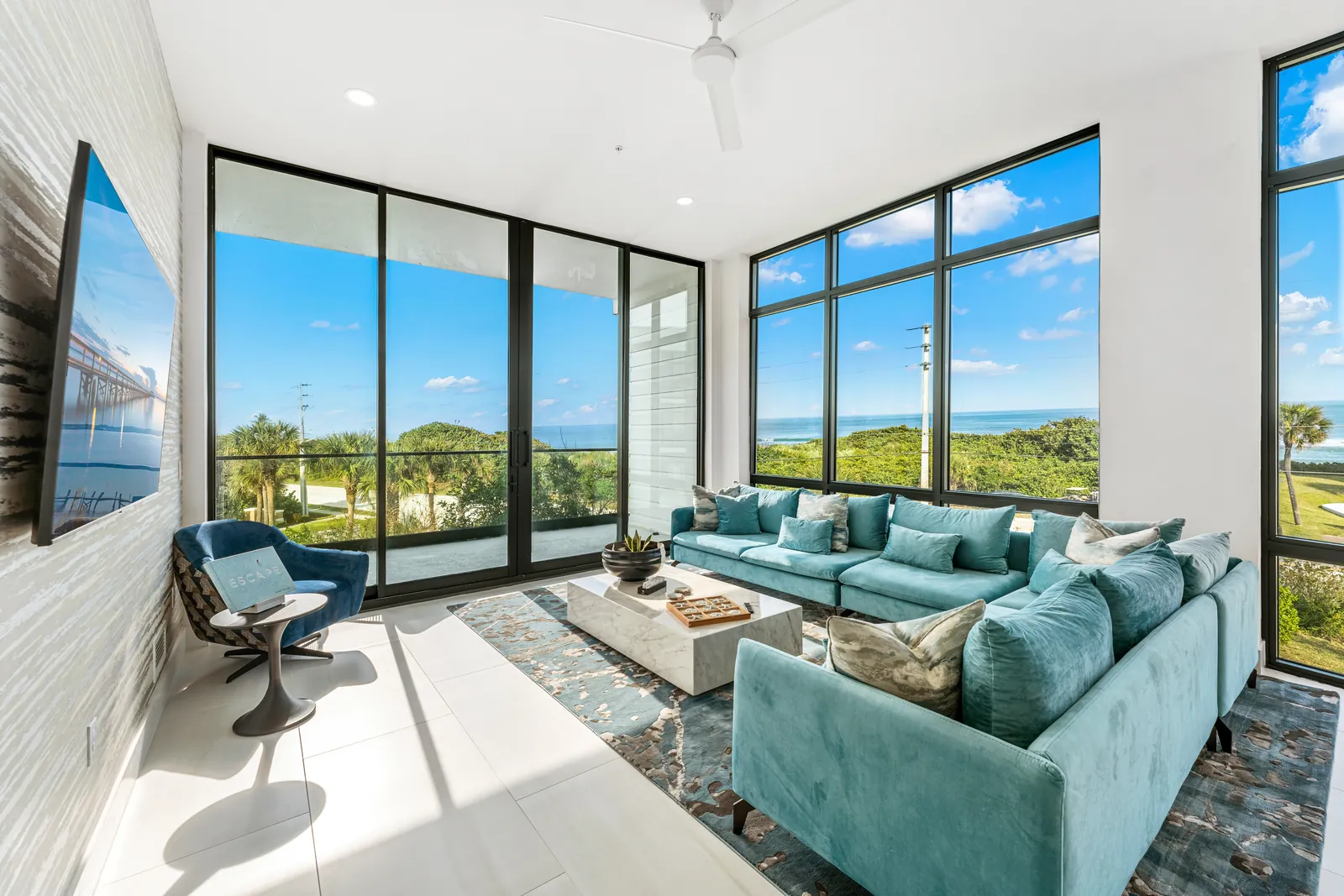 Glass-walled living room with turquoise seating and coastal views
