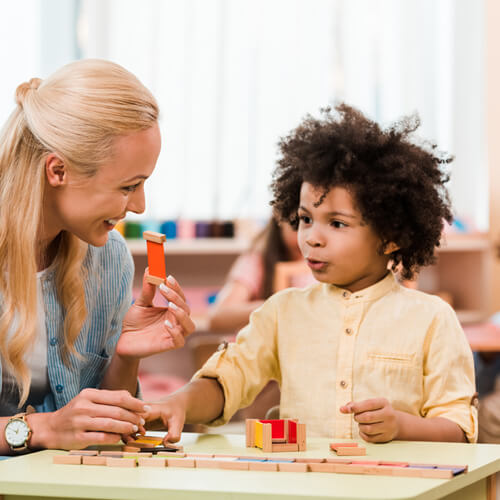 Teacher and young boy playing with wooden blocks