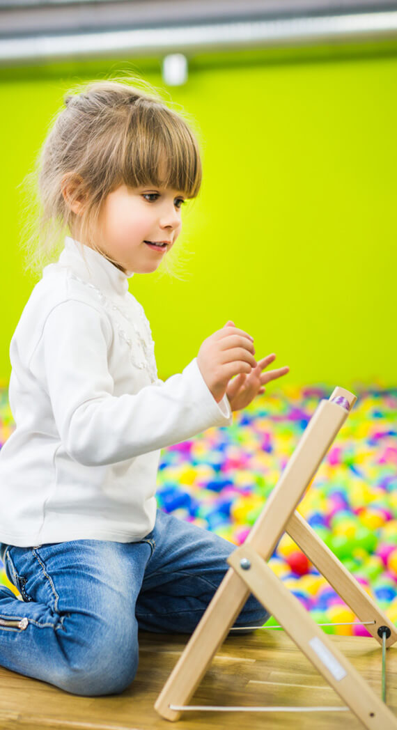 Young girl playing with wooden easel in colorful ballpit room